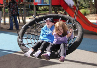 Inclusive playgrounds. Kids on swing. Photo. Touched by Olivia Foundation