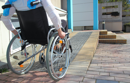 image of wheelchair user approaching building up a sloping brick path 