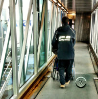 Image of airport assistant pushing wheelchair user on boarding bridge
