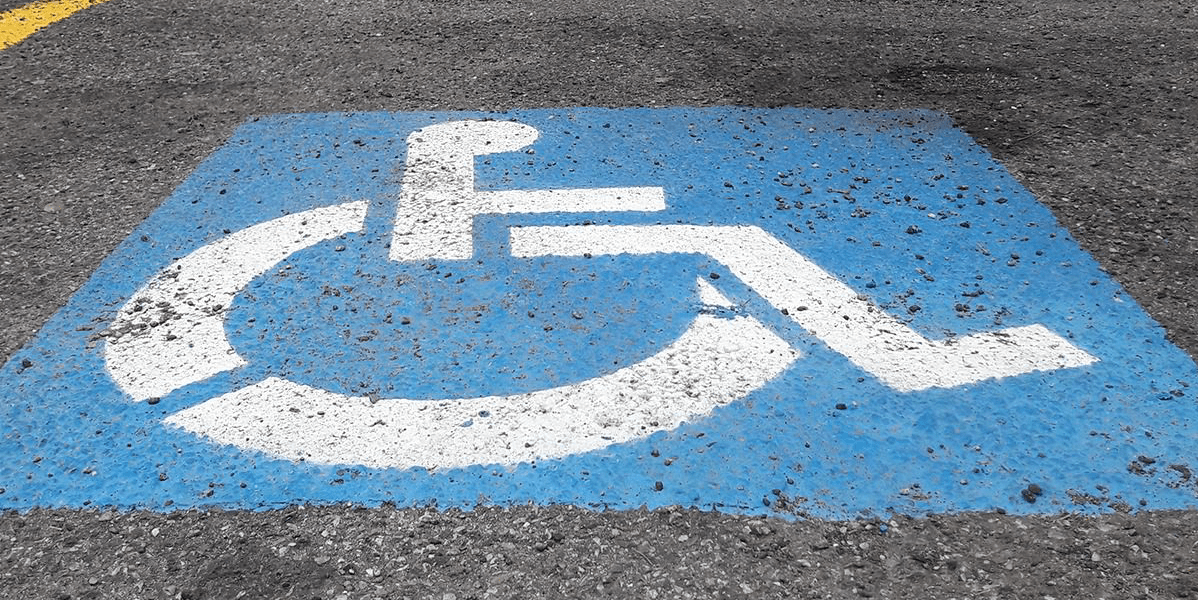 Photo of International Symbol of Accessibility painted in white on blue background on asphalt surface
