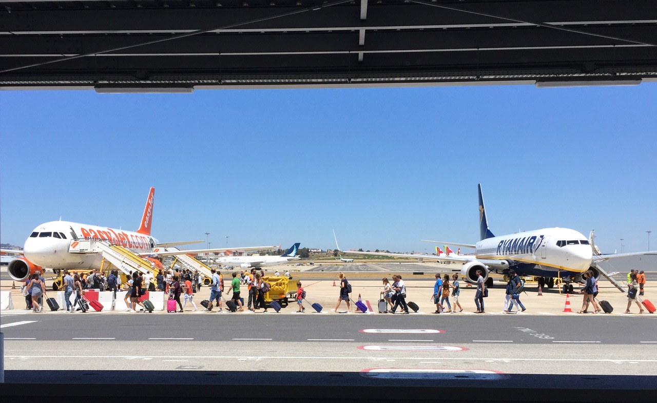 Summer-clad passengers cross the tarmac at Lisbon Airportt with EasyJet and Ryan Air planes in background